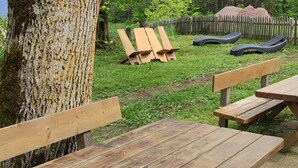 An outdoor wooden bench and picnic table set in a grassy area with a wooden fence and trees in the background. - Farm❤ (Eppan)