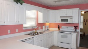 Cocina con armarios blancos, microondas, estufa y pileta.