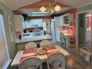 A dining area with a table set for four, surrounded by wicker chairs, a white tablecloth, and a centerpiece of fruit. - Venture Out, #402 North Marlin Dr. New amenities, WITH GOLF CART! (Panama City)