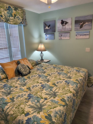 A bedroom with a bed, a nightstand, a lamp, and wall art. - Venture Out, #402 North Marlin Dr. New amenities, WITH GOLF CART! (Panama City)