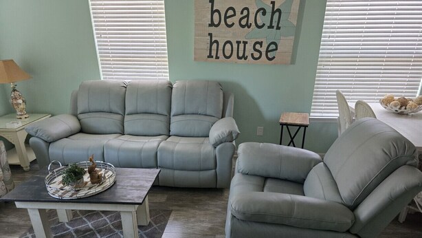 Una sala de estar con un sofá gris, un sillón a juego y una mesa de centro. Un letrero en la pared dice "beach house".
