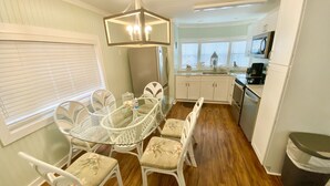 A compact kitchen with white cabinets, a dining area with a glass table and white chairs, and a trash bin. - Venture Out, #646 Octopus Dr. Comes WITH GOLF CART! (Panama City)