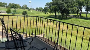 Un balcón con vista a un campo de golf, que incluye una torre de agua y árboles.