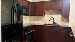 Una cocina con armarios de madera oscura, un refrigerador negro, un microondas y un lavamanos.