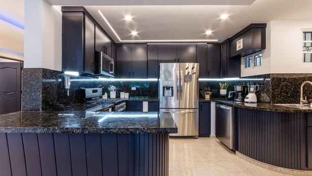 Uma cozinha moderna com armários escuros, bancadas de granito, eletrodomésticos de aço inoxidável e iluminação sob os armários.