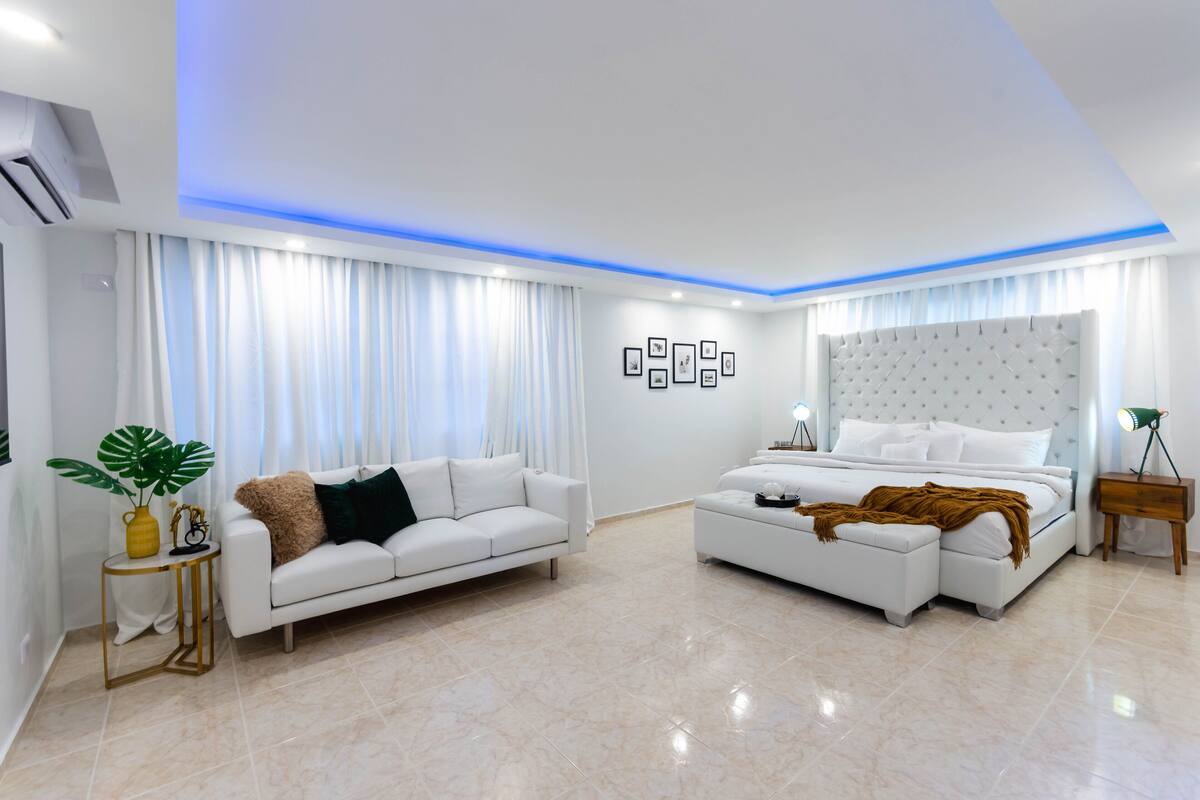 A modern bedroom with a bed, a sofa, a side table, and a lamp.