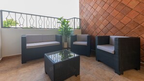 Varanda com móveis de vime, incluindo um sofá e duas cadeiras, além de uma mesa de centro de vidro.