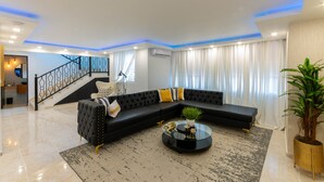 Uma sala de estar moderna com um sofá seccional preto, uma mesa de centro de vidro e uma escada que leva a outro andar.