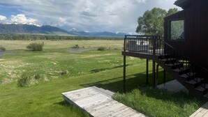 A wooden cabin with a deck and a view of a mountainous landscape. - Spring Creek Guest House (Ennis)