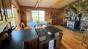 A kitchen with wooden cabinets, a stove, and a stone wall. - Spring Creek Guest House (Ennis)
