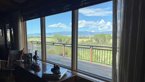 A room with large windows overlooking a deck and mountains. - Spring Creek Guest House (Ennis)