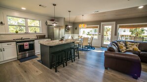 Una cocina moderna con una isla central, taburetes de bar y un comedor con vistas al exterior.