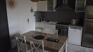 Kompakti keittiö, jossa on valkoiset kaapit, pesuallas ja astianpesukone. Keittiössä on ruokapöytä tuoleineen sekä koristeellinen seinäkello.