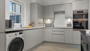 A modern kitchen with built-in appliances, a washing machine, and a large window. - Cottage Mews - Seaside Cottage, Parking, Terrace (Tenby)