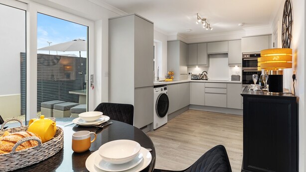 A modern kitchen with a dining area, a washing machine, and a large window. - Cottage Mews - Seaside Cottage, Parking, Terrace (Tenby)