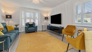 A modern living room with a sofa, armchairs, a TV, and a chandelier. - Cottage Mews - Seaside Cottage, Parking, Terrace (Tenby)