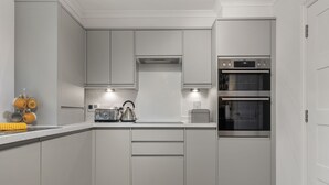 A modern kitchen with white cabinets, a built-in oven, and a coffee maker. - Cottage Mews - Seaside Cottage, Parking, Terrace (Tenby)