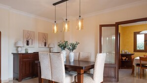 A dining area with a wooden table, six patterned chairs, a vase with plants, and pendant lights. - Charming Villa Can Albons in Porto Colom for 8 people (Portocolom)