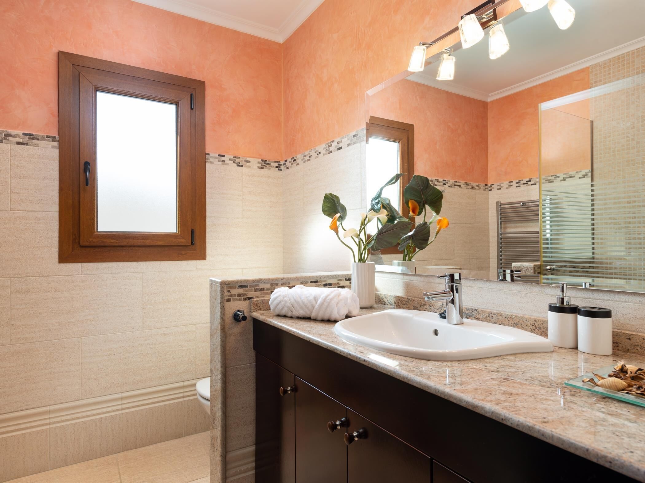 Une salle de bain dotée d’un grand miroir, d’un lavabo et d’un meuble-vasque avec des placards de couleur sombre.