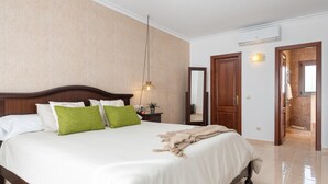 A hotel room with a large bed, a wooden headboard, a bedside table with a lamp, a mirror, and a door leading to a bathroom. - Charming Villa Can Albons in Porto Colom for 8 people (Portocolom)