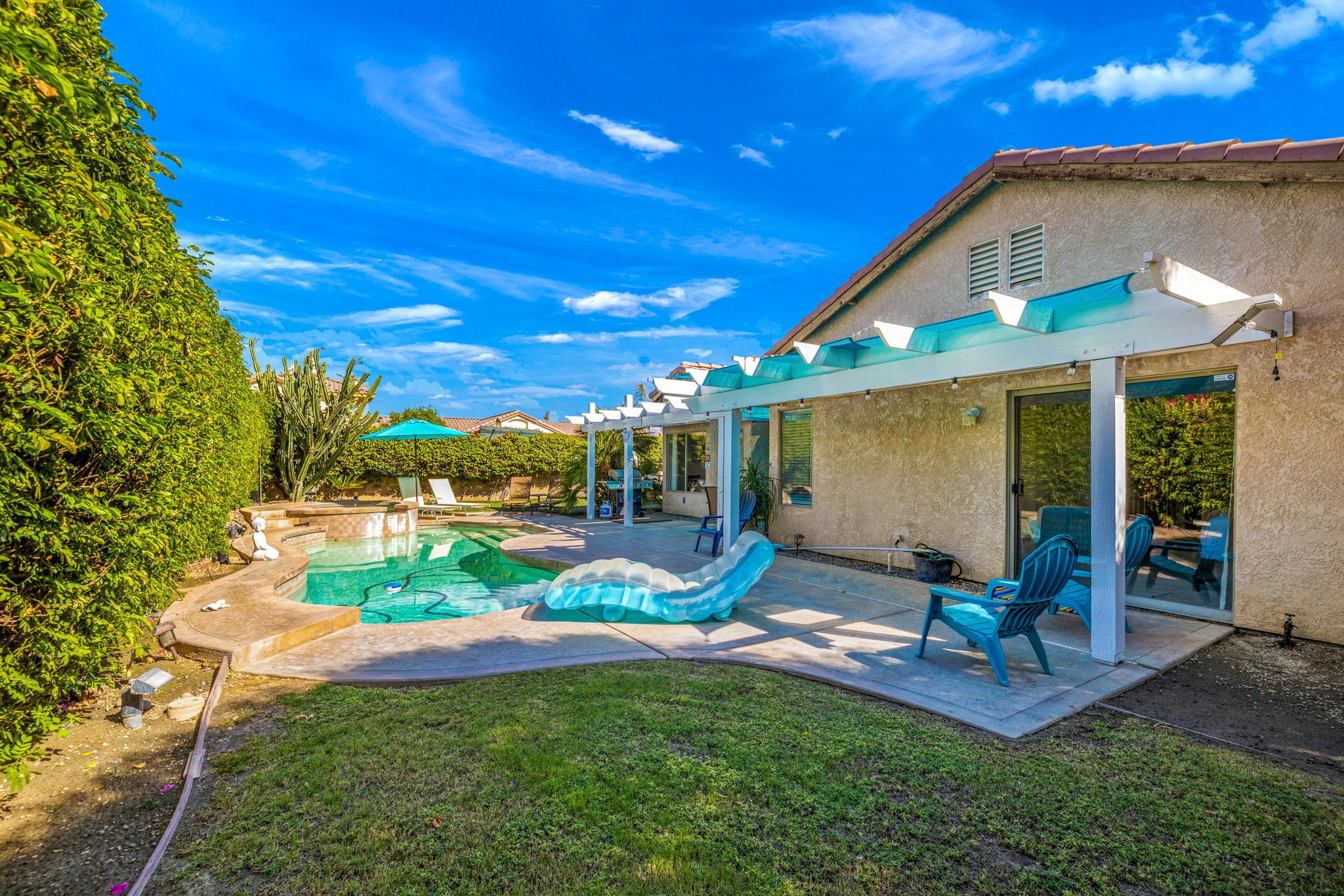 A backyard with a swimming pool, a covered patio, and outdoor seating.