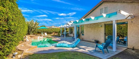 A backyard with a swimming pool, a covered patio, and outdoor seating.