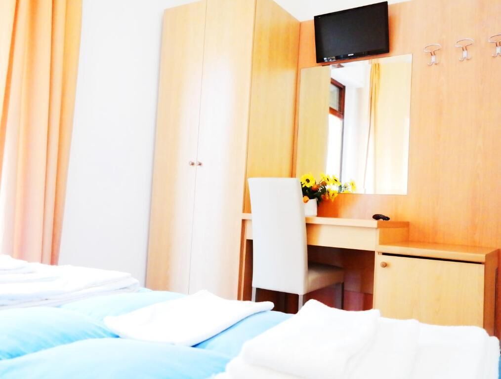 A hotel room with a bed, a desk, a mirror, and a television.