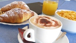 A breakfast setting with croissants, a cup of coffee, a glass of orange juice, and a bowl of cereal. - Central Plaza (Lecce)
