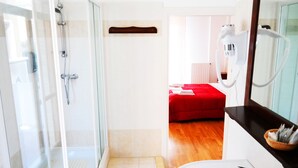 A modern bathroom with a glass shower enclosure, a white sink, and a red bed in the adjacent room. - Central Plaza (Lecce)