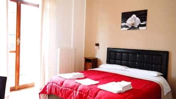 Una camera d'albergo con un letto, una coperta rossa, cuscini bianchi, un quadro di un fiore al muro e una finestra con tende.