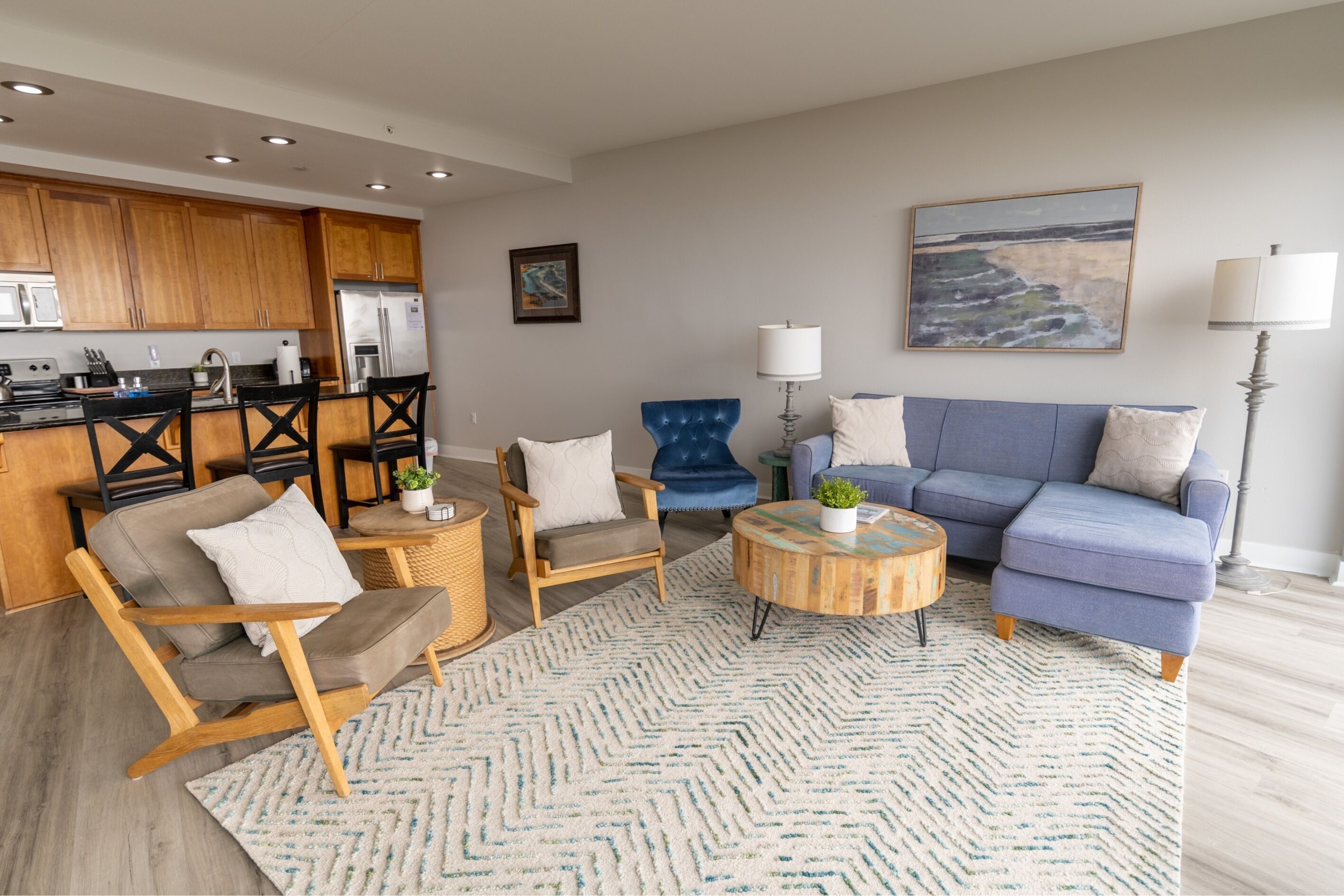 Ein modernes Wohnzimmer mit einer Couch, Sesseln, einem Couchtisch und einer Küchenzeile mit Holzausbau und Geräten.