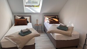 Una habitación pequeña y moderna con dos camas, una mesita y un ventanal.