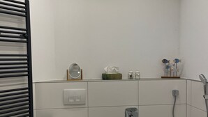 Un baño moderno con inodoro, bañera y ducha. Hay artículos de aseo en la pared y un perchero para toallas.