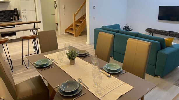 Una sala moderna con comedor, un sofá, un televisor y una escalera.