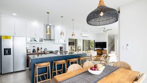 Una cucina moderna con mobili bianchi, un'isola centrale con sgabelli da bar, un tavolo da pranzo con tovaglia americana e un ampio lampadario a sospensione.