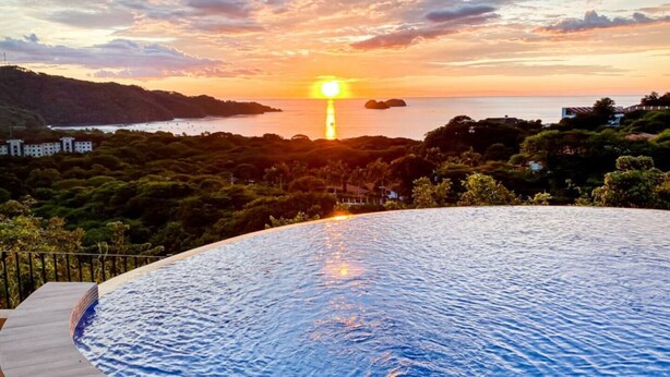 Una piscina con vista sul tramonto, immersa nel verde e circondata da colline.