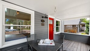 A covered porch with a dining table and chairs, a red door, and a view of the street. - Agatha Stecker cottage - Historic Miner’s cottage (Louisville)