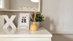 A white desk with a large white 'X' and a framed picture with a symbol. A yellow vase with a plant and reed sticks is on the desk.