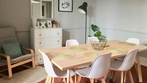 A dining area with a wooden table, white chairs, a white dresser, a mirror, and a plant.