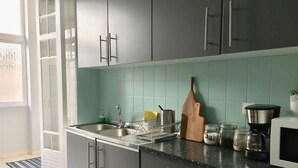 A kitchen with grey cabinets, a black countertop, a wooden cutting board, a coffee maker, and a jar of spices.