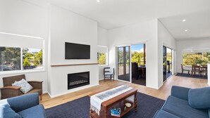 Amplia sala de estar con chimenea, televisor y comedor con vistas al exterior.