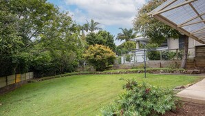 Ein gepflegter Garten mit Rasen, verschiedenen Bäumen und einer Metall-Pergola.