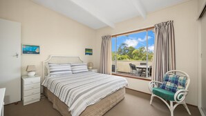 Ein Schlafzimmer mit Bett, Nachttischen, einem Sessel, einem Fenster mit Vorhängen und Bildern an den Wänden.
