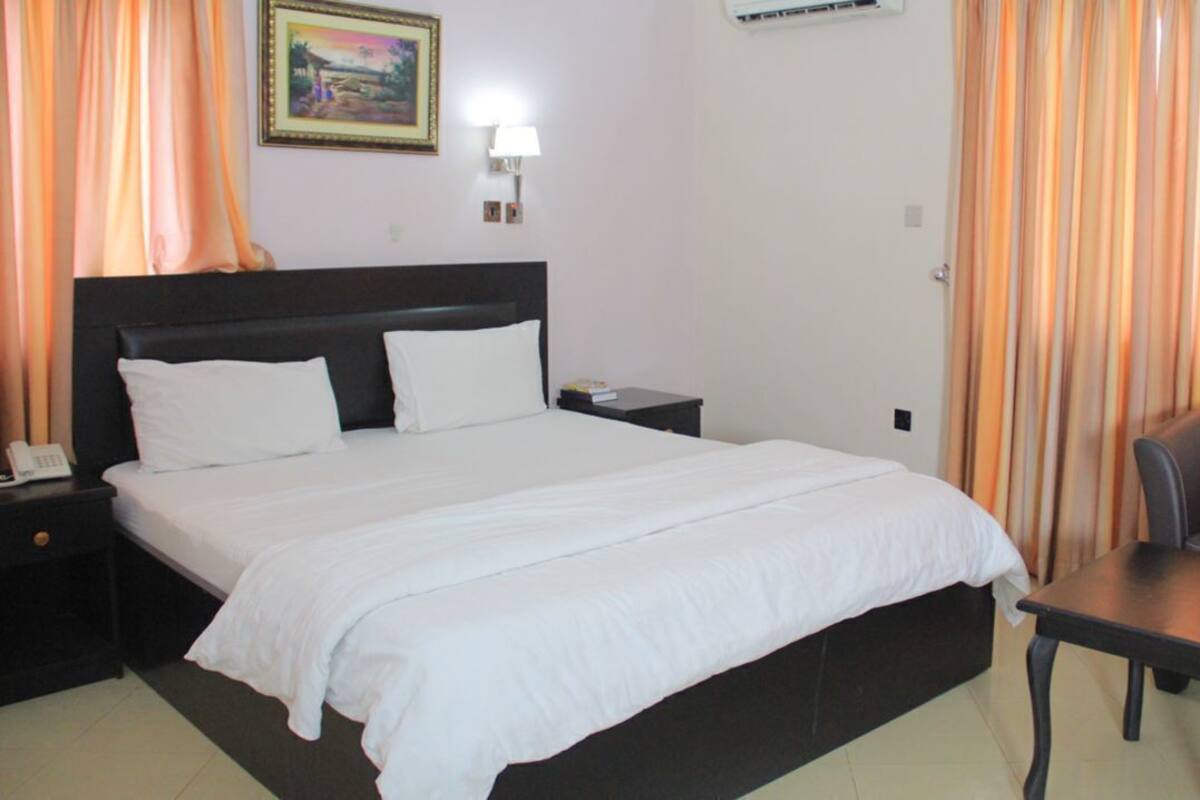 A hotel room with a bed, bedside table, lamp, and a chair.