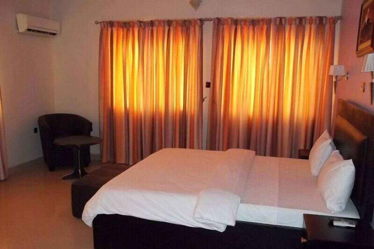 A hotel room with a bed, a chair, a small table, and curtains.