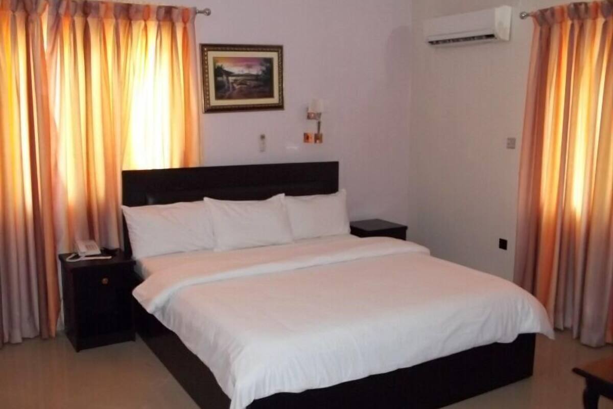 A hotel room with a large bed, a bedside table with a phone, and curtains.