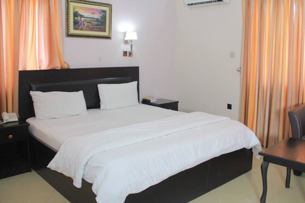 A hotel room with a bed, bedside table, lamp, and a chair.