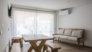 A living room with a wooden table, benches, a sofa, and a large window with sheer curtains. - Porch House (Braga)