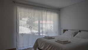 A bedroom with a large bed, white curtains, and a wooden floor. - Porch House (Braga)