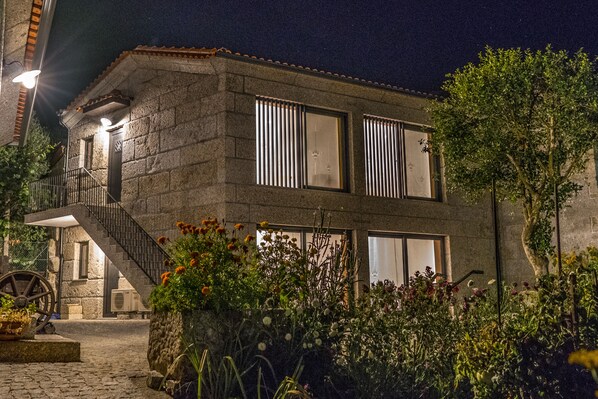 A stone building with a staircase, large windows, and a garden with flowers.